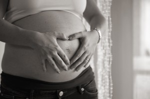 Schwangere Frau formt mit den Händen ein Herz auf ihrem Bauch
