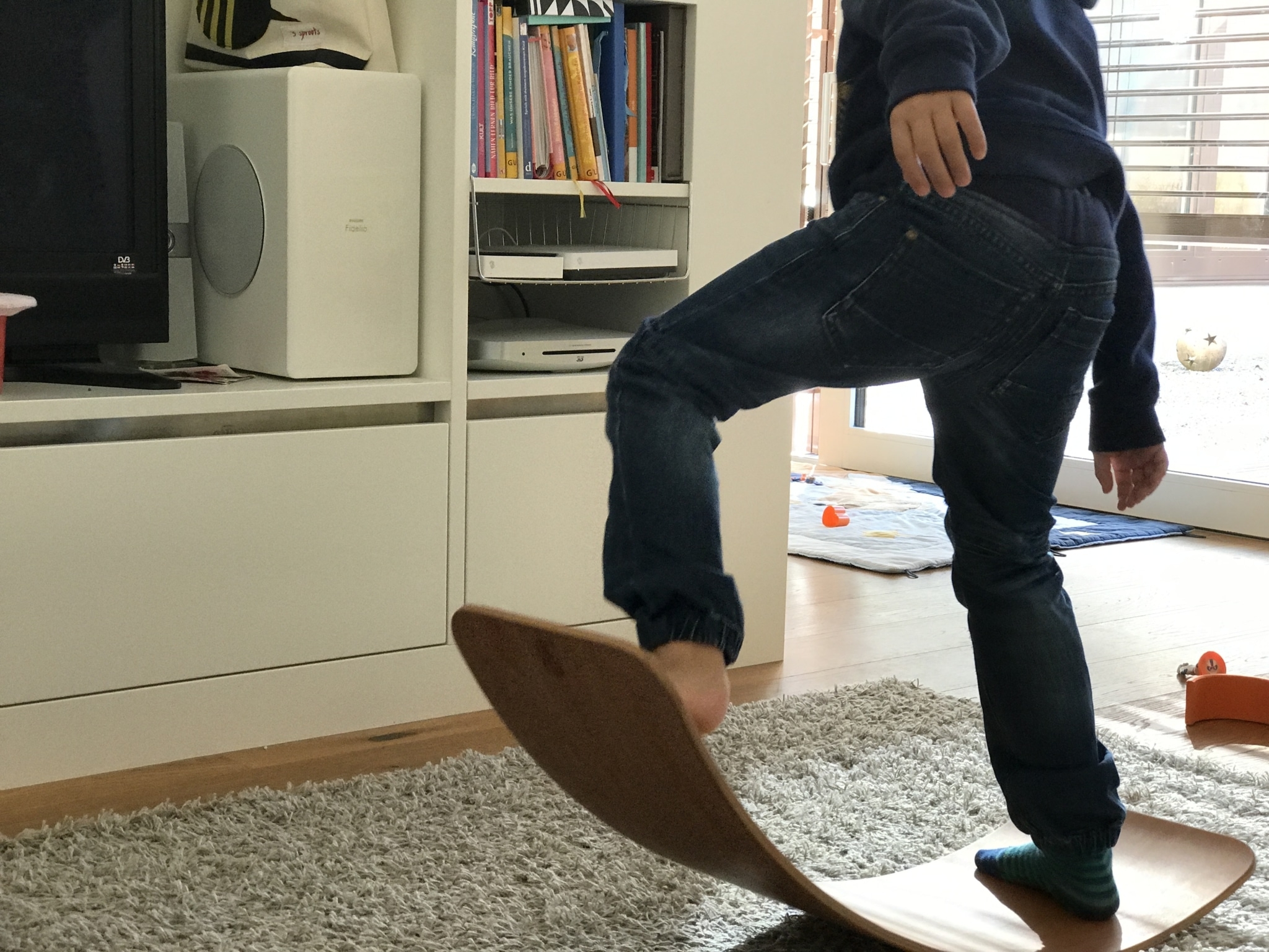 Junge balanciert auf einem gebogenen Brett auf einem Teppich im Wohnzimmer