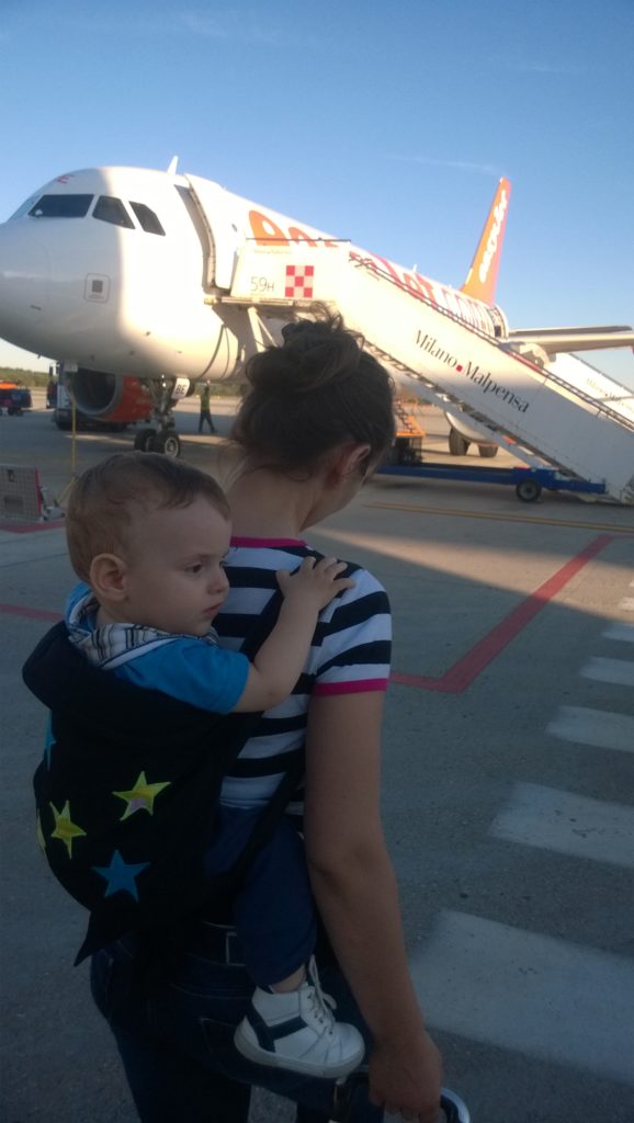 babywearing mama in front of an airplane