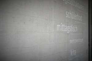 Richtungsweiser an der Wand, weisse Schrift auf Beton zeigen Richtung Kita, Schülerhort etc.